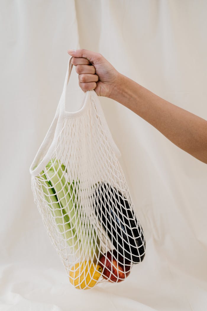Hand holding a reusable mesh bag filled with colorful fresh vegetables, promoting zero waste lifestyle.